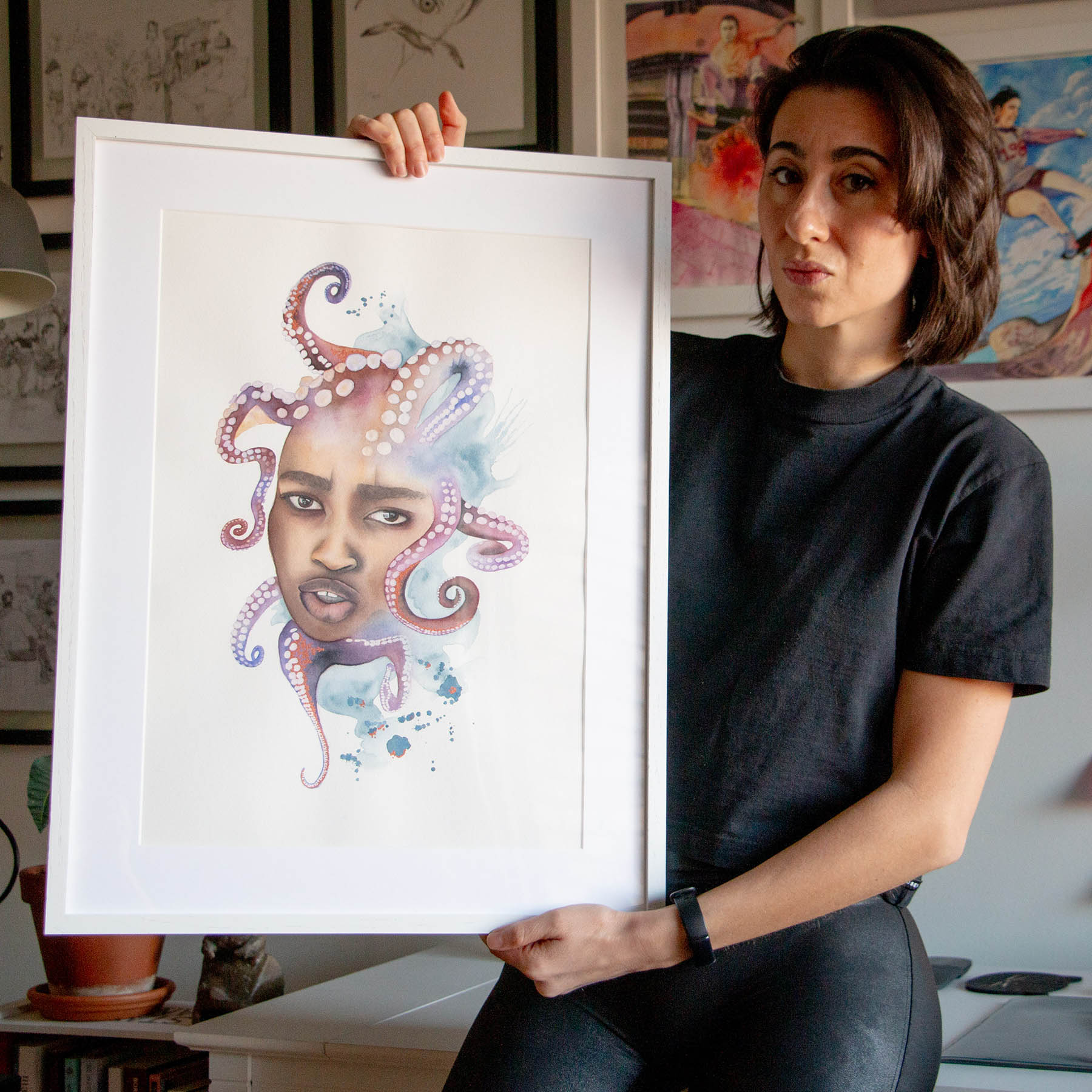 Artist Paula Di Marco holding her original framed watercolor painting 'Tangled'—a surreal portrait of a woman entwined with vivid octopus tentacles. Photographed in her studio, this emotionally charged piece is part of Paula’s mystical watercolor collection centered on emotional healing and transformation.