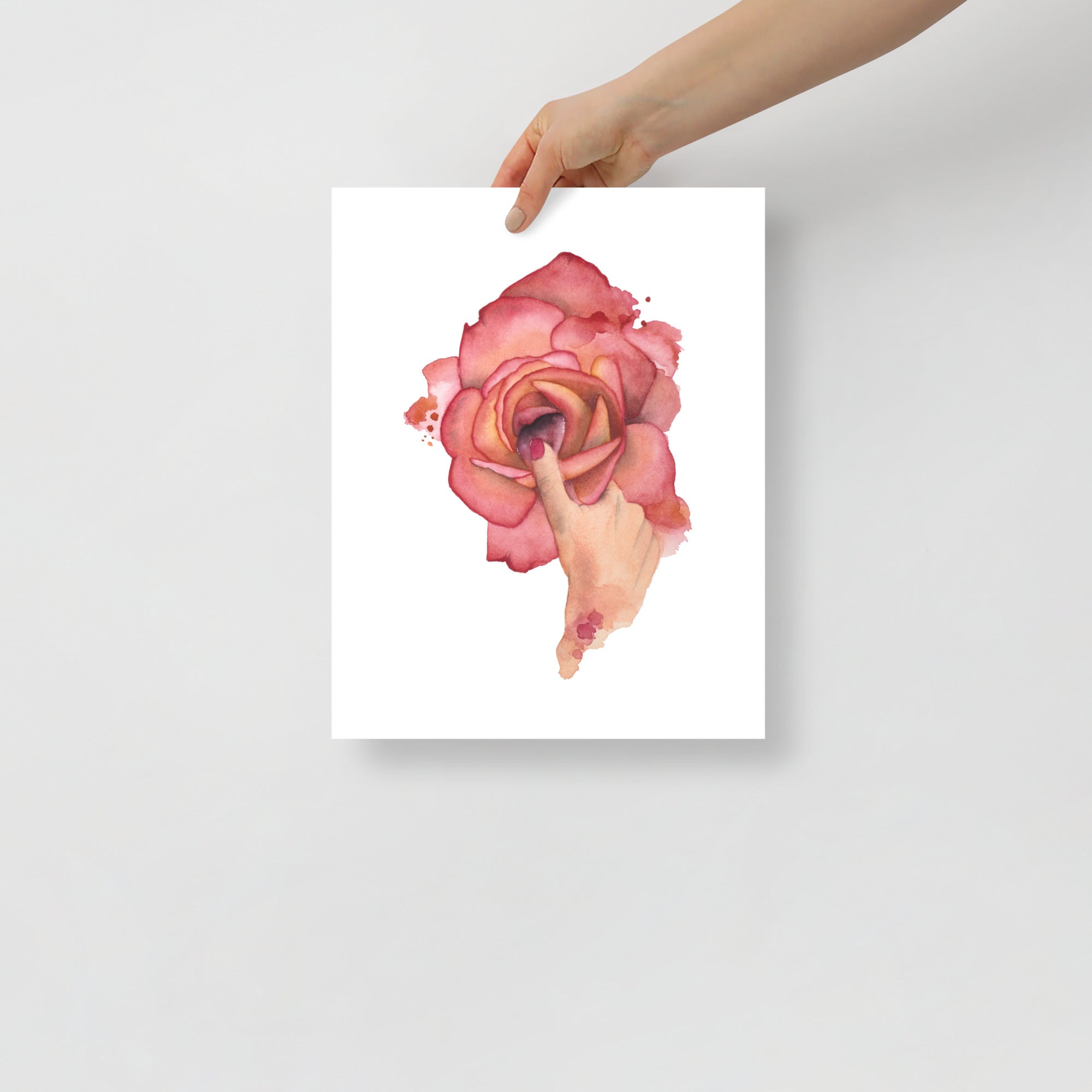 Hand holding an 11x14 surrealist watercolor art print featuring a sensual rose and finger gesture – part of the Playful Awakening collection by Paula Di Marco
