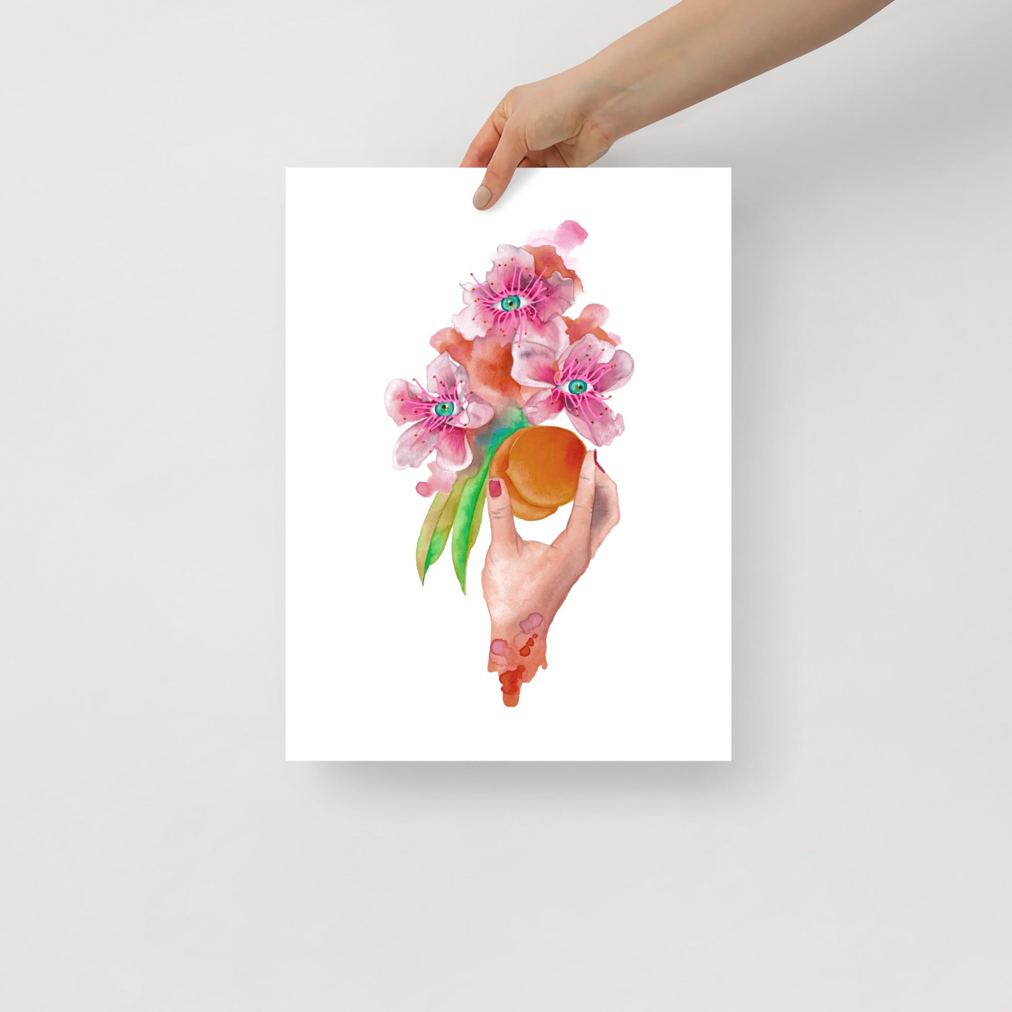 Hand holding ‘Forbidden Fruit’ giclée print by Paula Di Marco — a surreal watercolor artwork featuring pink blossoms and a ripe peach, symbolizing sensual awakening. Unframed poster held against a light background.