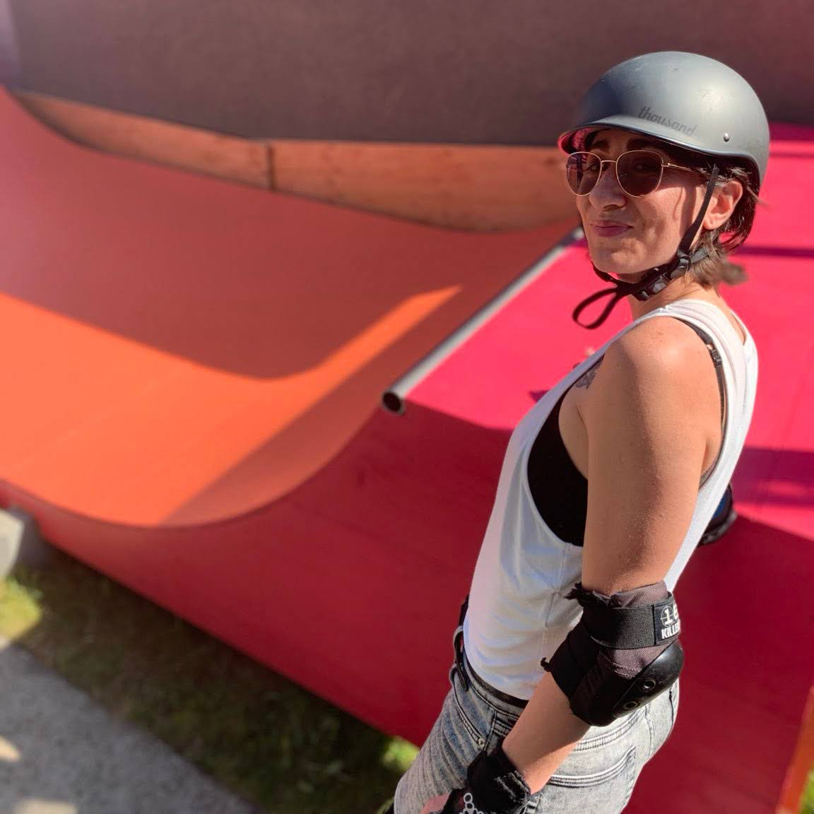 Paula beside a skateboarding ramp with a tank top, helmet and sunglasses on