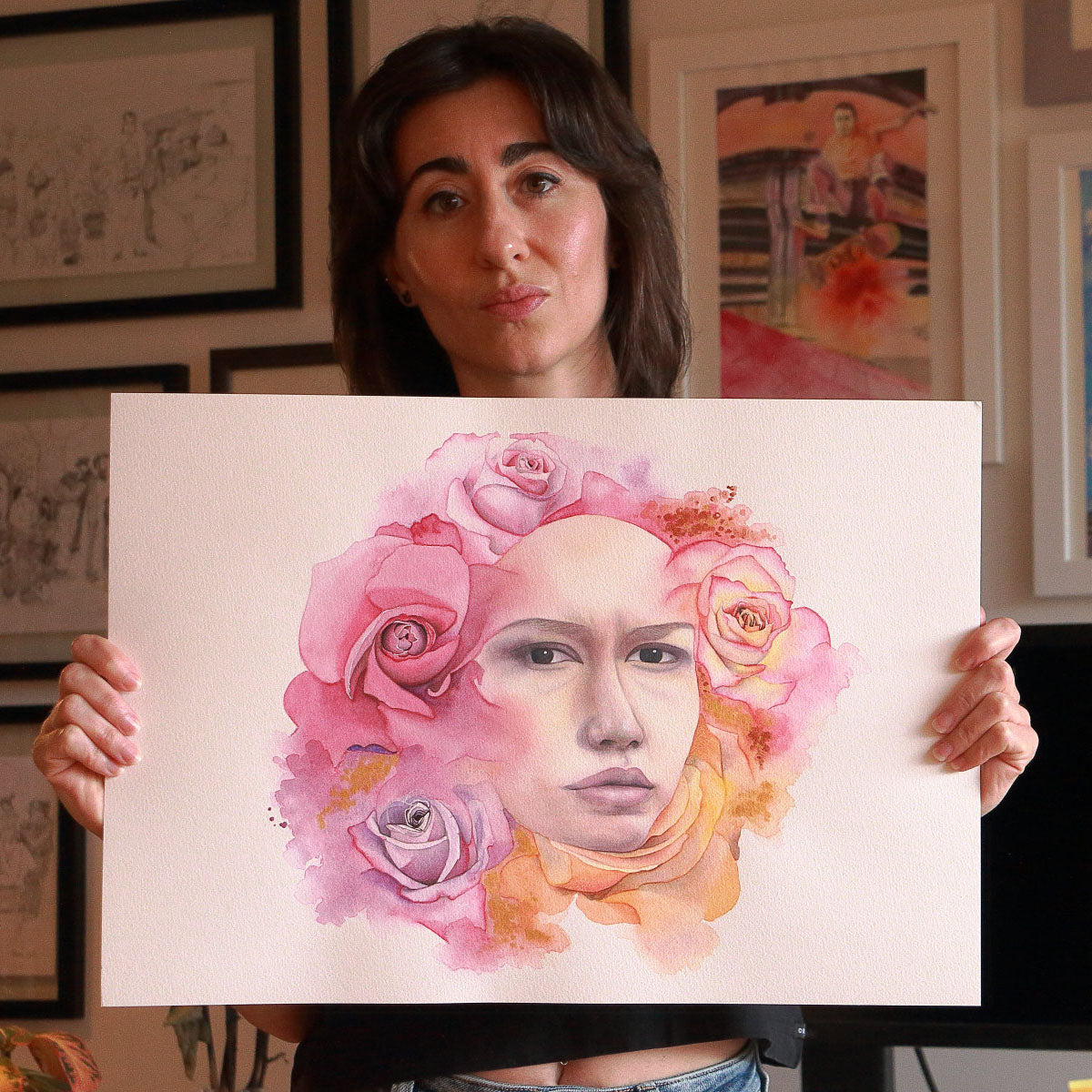 Artist Paula Di Marco holding her original watercolor painting 'A Quiet Moment'—a surreal portrait of a woman surrounded by vibrant pink, peach, and lavender roses. Captured in her studio, this emotionally charged piece is part of her mystical watercolor collection for emotional healing and introspection.