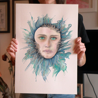 Artist Paula Di Marco holding her original watercolor painting 'Drowning'—a surreal portrait of a woman immersed in deep teal waves, symbolizing grief, overwhelm, and emotional release. Photographed in her studio, this piece is part of her mystical watercolor wall art collection for healing and introspection.